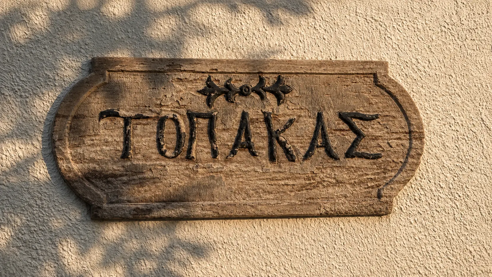 Η σκαλιστή ξύλινη πινακίδα «Τοπακάς» στον τοίχο του σπιτιού